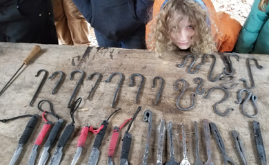 Homeschool blacksmithing student with variety of objects made in class