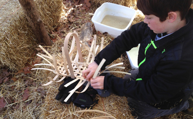 Crafty Critters camper weaving a basket in the forest at summer camp in Asheville