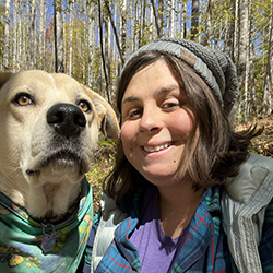 Nature connection mentor Caitlan Feild sits beside her dog in the woods