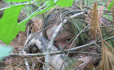 Child hiding in the forest learning stealth and natural camouflage at summer camp