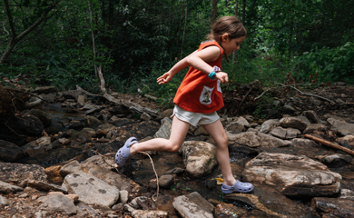 Girl running across creek in the forest at outdoor homeschool day program