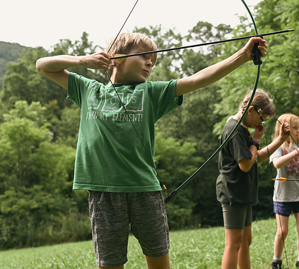 Confident young camper siting down range with an arrow drawn at archery camp