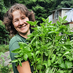 Child educator and camp counselor Emily Lutken poses outdoors hugging a large potted plant