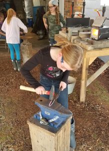 Teenage girls working with hammer and anvil at blacksmithing camp