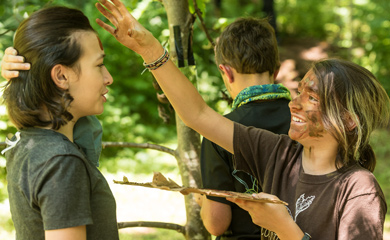Mature homeschool students painting camouflage on each other's faces at nature school