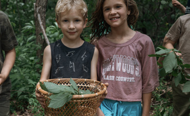 Two children holding a basket of leaves they have collected at foraging camp