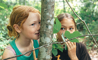 Kids-enjoying-forest-experience-at-Asheville-homeschool-class Two young girls at Asheville homeschool class in the forest kidding around