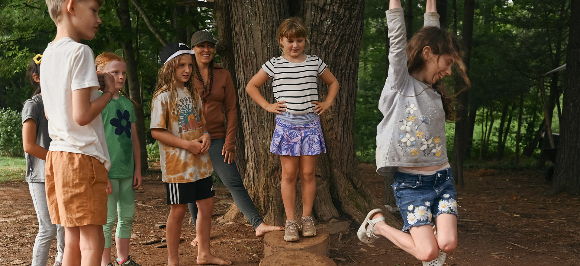 Kids playing at the forest edge standing on stumps and swinging from tree branches