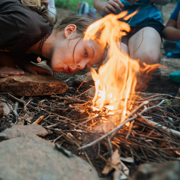Girl blowing on a campfire getting it started at camp
