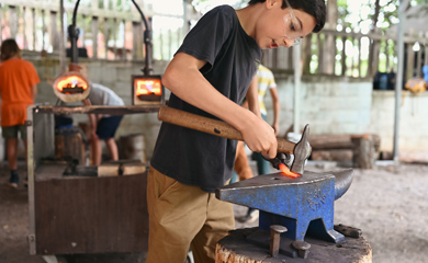 Boy working with hammer and anvil and hot glowing iron at Asheville homeschool craft class