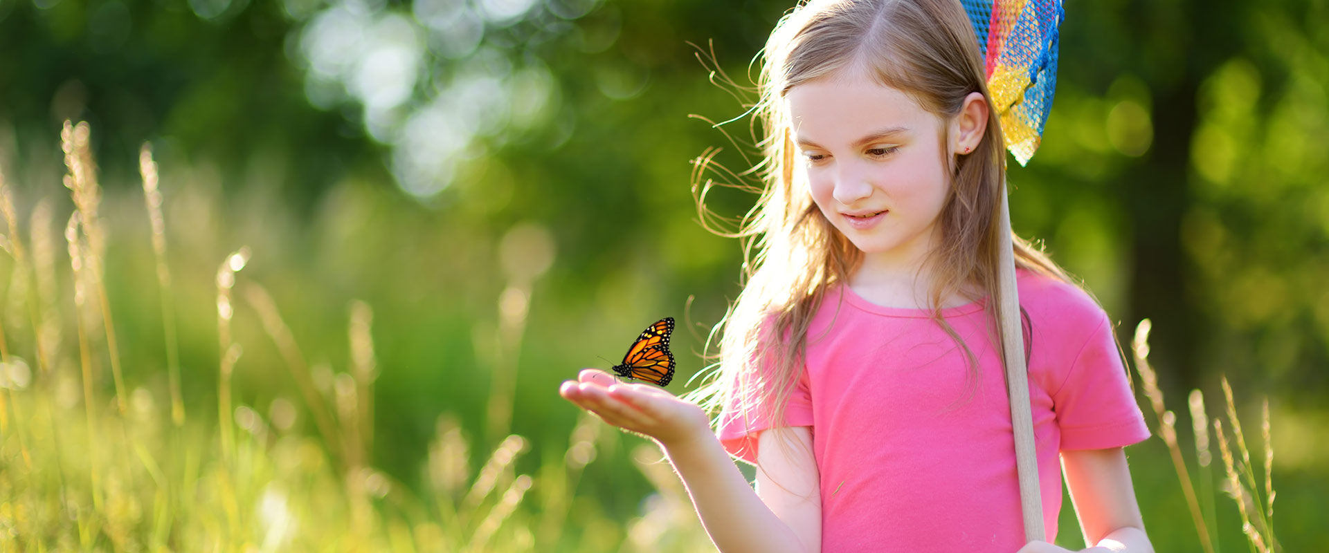 Young girl at forest's edge with a monarch butterfly resting on her outstretched hand at nature school