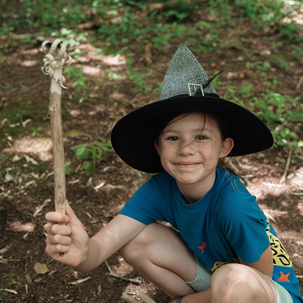 Young wizard showing off their in-progress wand carving project at forest school summer camp
